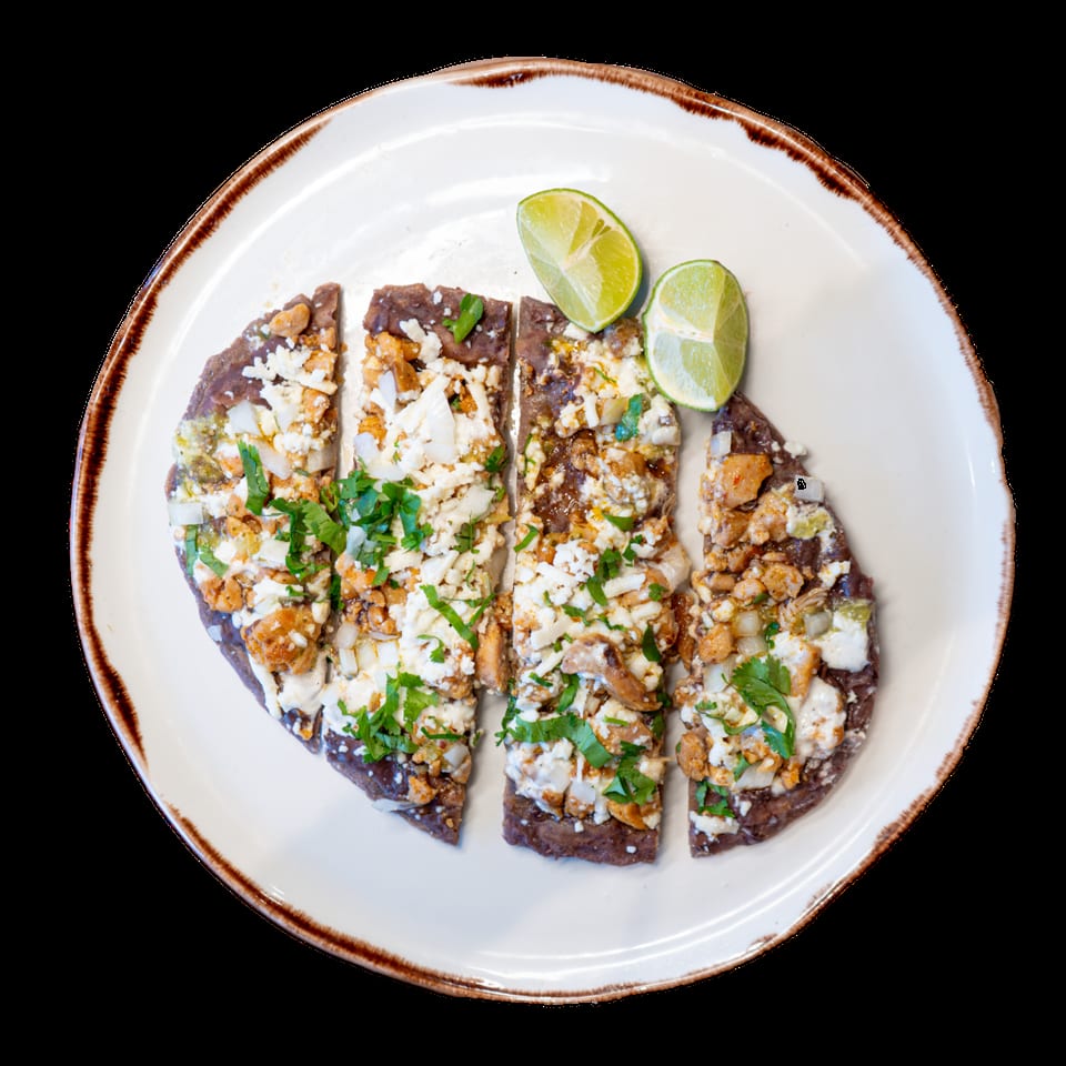 Four slices of bean and cheese flatbread with cilantro and lime wedges on a white plate.