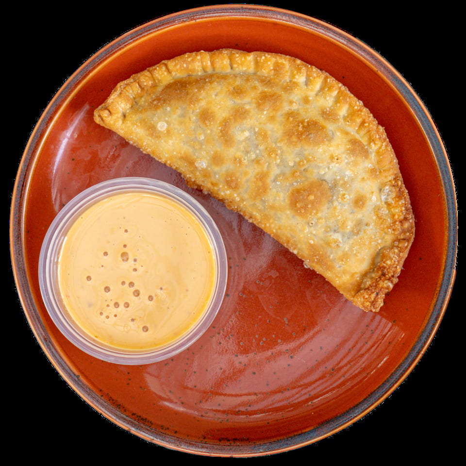 Golden-brown fried empanada on a rustic orange plate with a side of creamy dipping sauce.