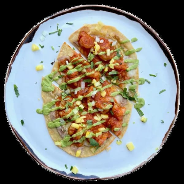 Overhead view of a shrimp tostada with red sauce, green drizzle, and diced mango on a white plate.