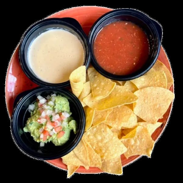A red plate with tortilla chips, guacamole, salsa, and queso dip in black bowls.