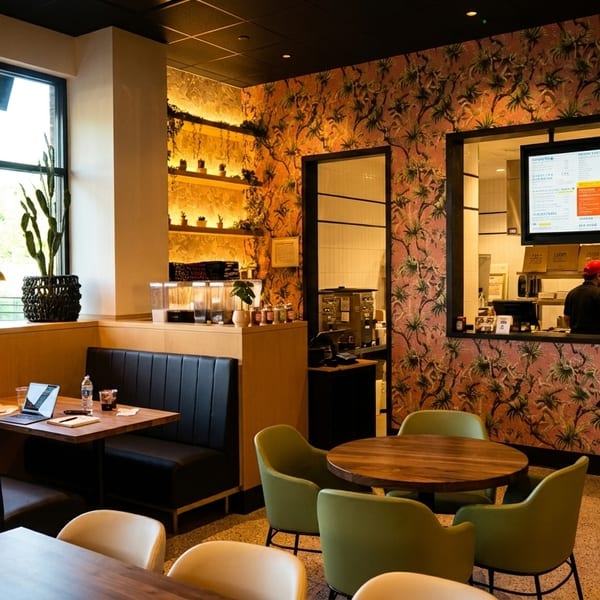 Modern restaurant interior with booths, tables, a large window, and staff visible through a kitchen pass-through.